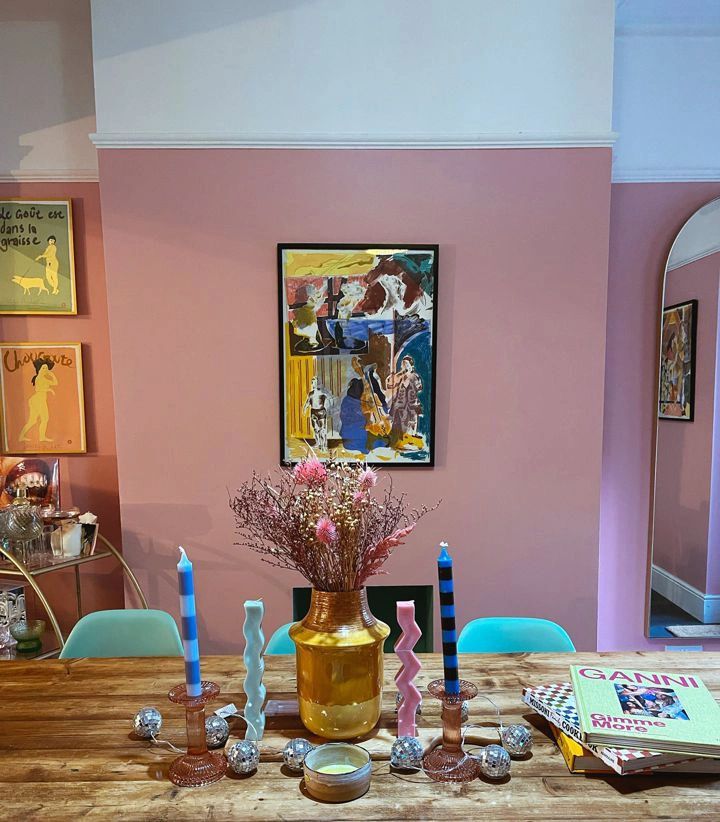 a wooden table topped with a vase filled with flowers next to blue chairs and pictures on the wall