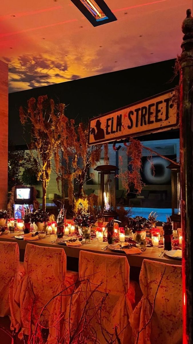 a long table with many candles on it in front of a building and an orange sky