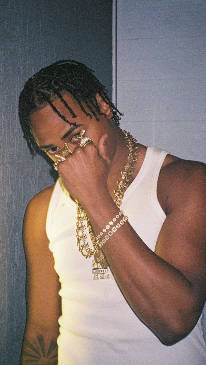 a young man wearing gold chains and holding his hand to his face while standing in front of a door