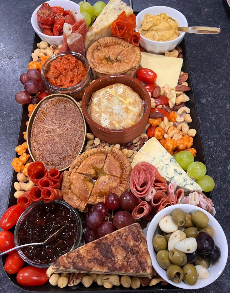 a table topped with lots of different types of cheeses and crackers next to bowls of olives