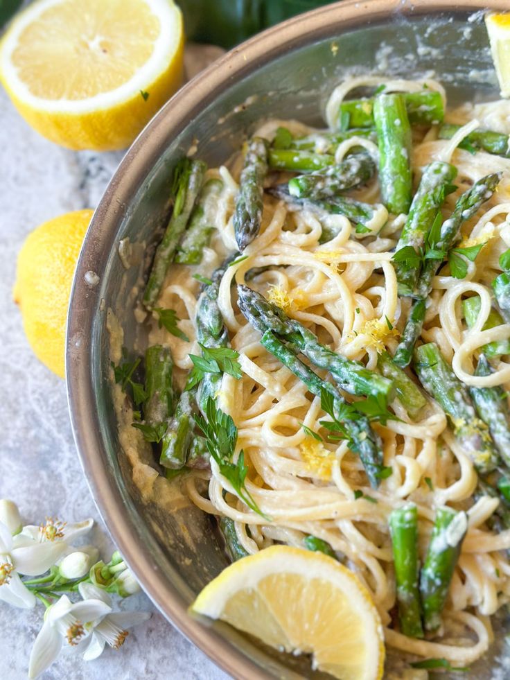 a bowl filled with pasta and asparagus on top of a table next to lemons