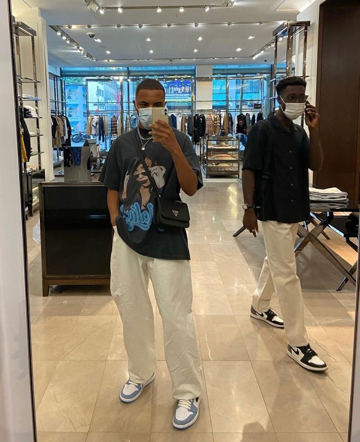 two men wearing face masks in a clothing store looking at their cell phones and taking pictures