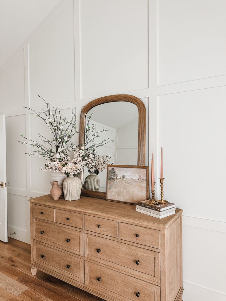 a wooden dresser topped with a mirror and vase filled with flowers on top of it