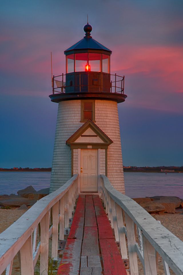 a light house sitting on top of a wooden pier next to the ocean at sunset