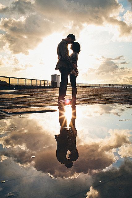 a couple kissing in front of the sun with clouds reflected on the water and sky