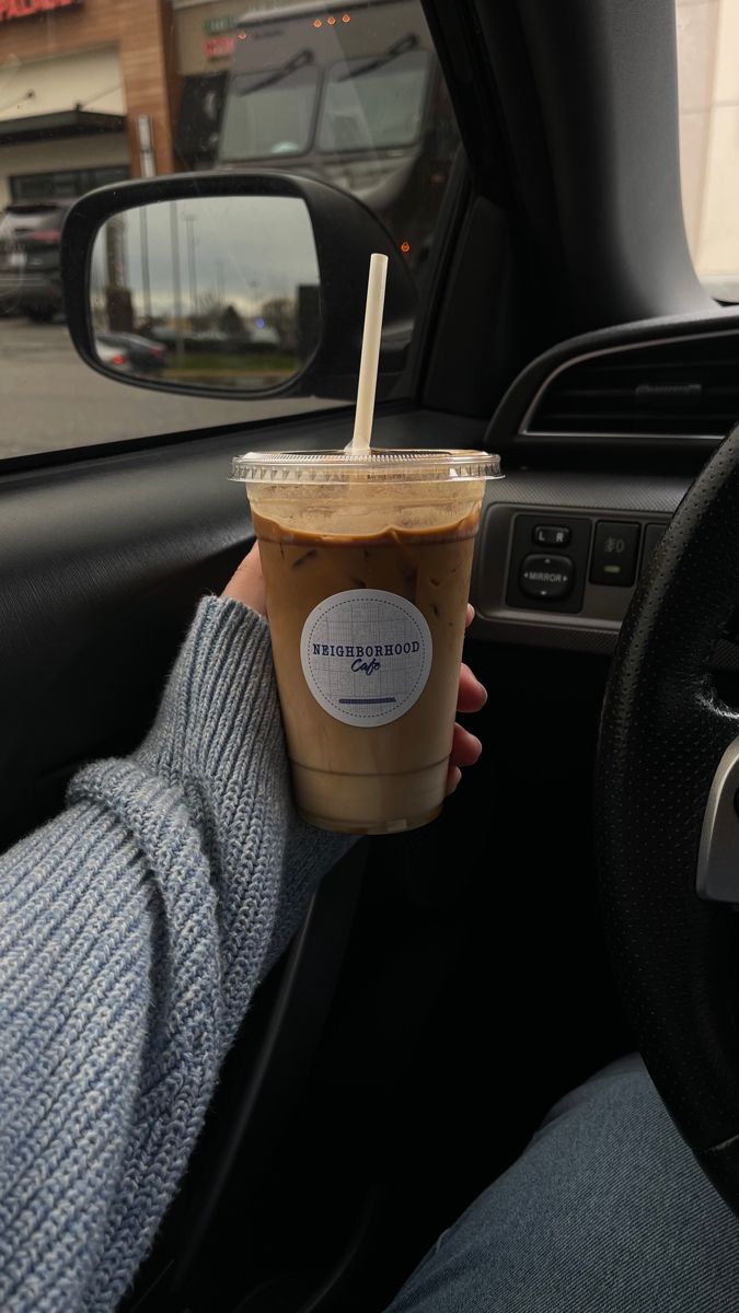 a person holding up a cup of coffee in the drivers seat of a car while driving