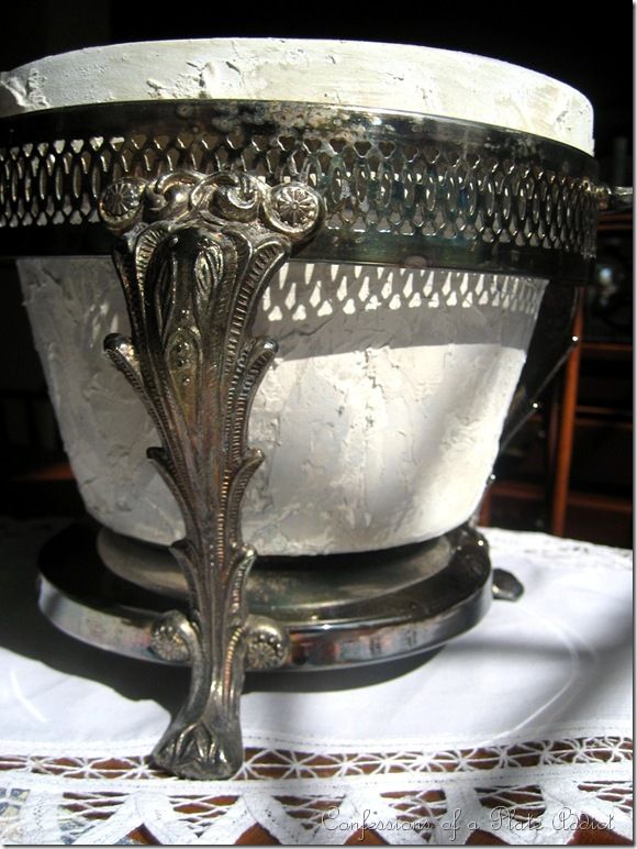 an ornate silver bowl sitting on top of a white tablecloth covered table with doily