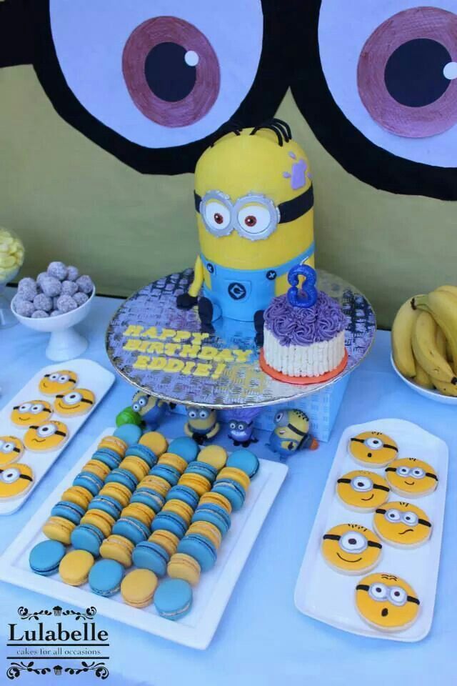 a table topped with cakes and desserts covered in minion faces next to bananas