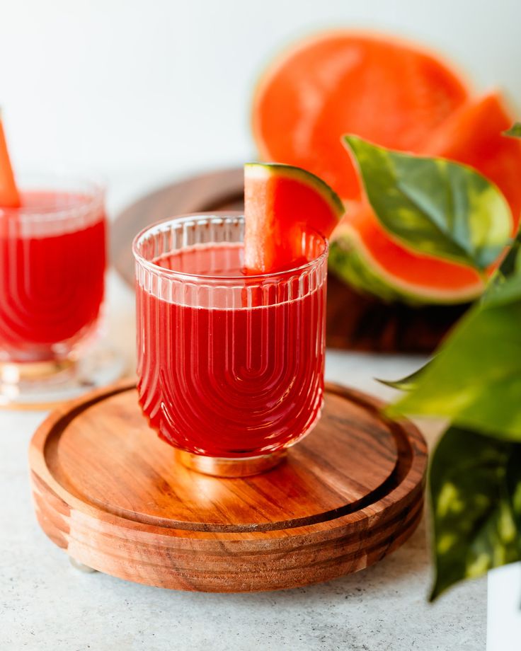 two glasses filled with red liquid sitting on top of a wooden tray next to sliced oranges