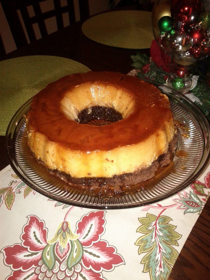 a cake sitting on top of a glass plate next to a christmas tablecloth and tree