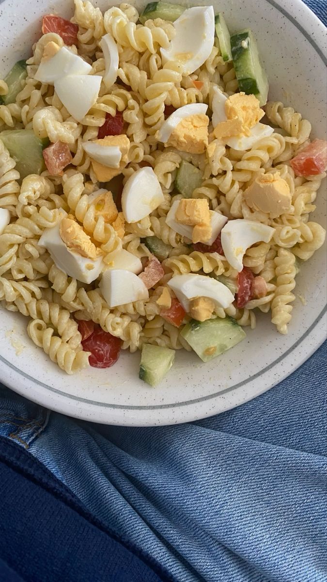 a white bowl filled with pasta and veggies on top of a blue cloth