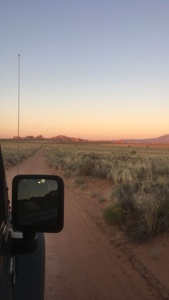 the sun is setting on a dirt road in the middle of nowhere, with mountains in the distance