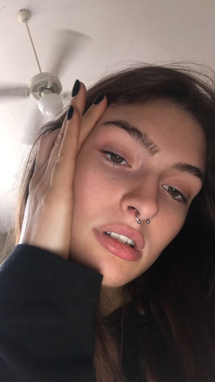 a young woman with piercings on her nose is holding her hand to her face