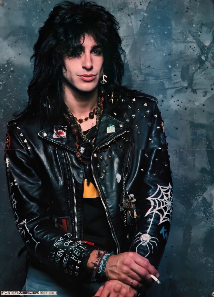 a man with black hair wearing a leather jacket and bracelets, posing for the camera