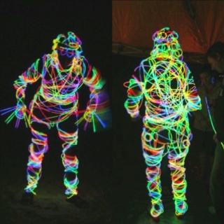 two people are standing in the dark with colored lights on their body and arms, one person is holding a cell phone