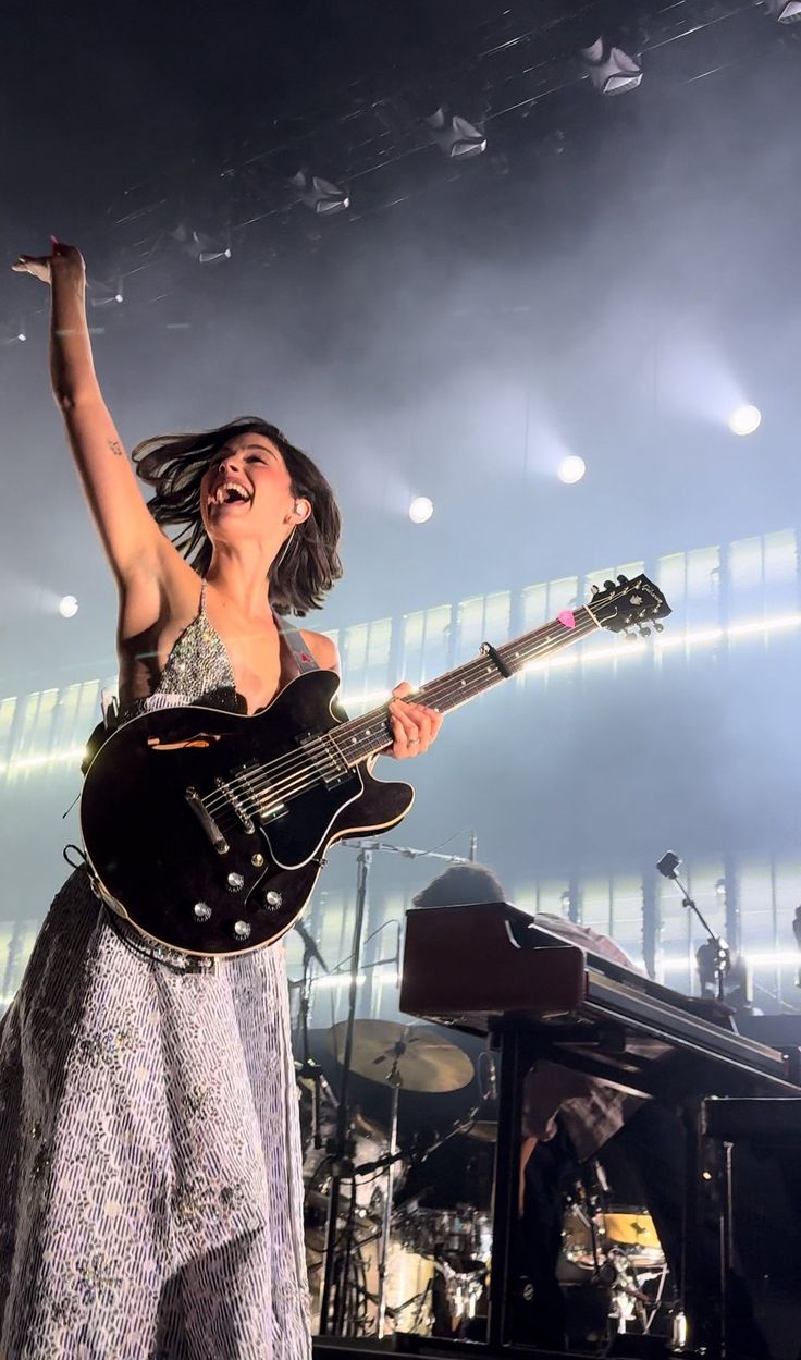 a woman in a dress is holding her guitar and singing into the microphone on stage