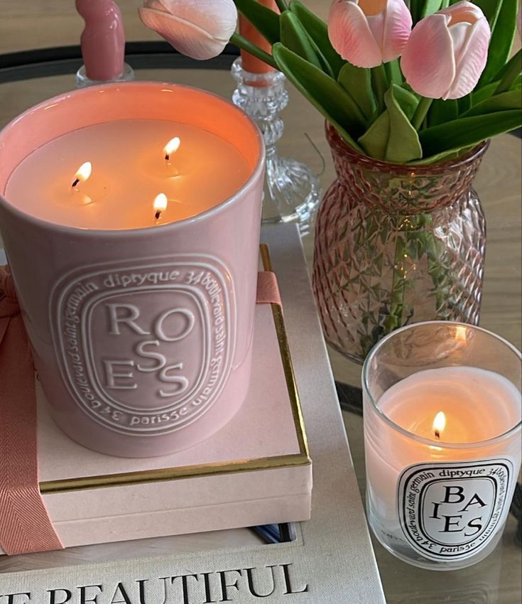 a pink candle sitting on top of a table next to a book and vase with flowers