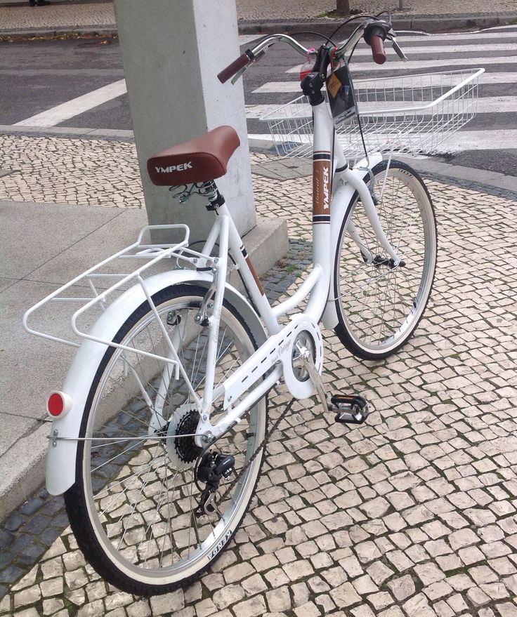 a white bicycle parked next to a pole on a sidewalk with a basket in the front