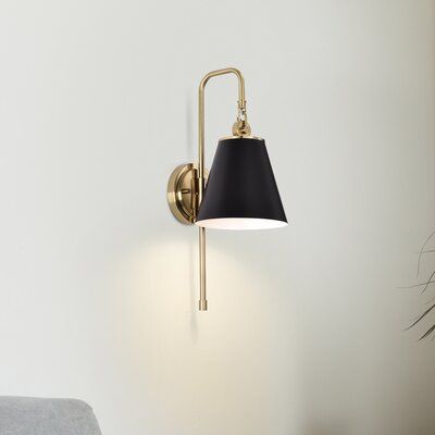 a wall light with a black shade on it next to a chair and potted plant