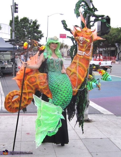 a woman is dressed up as a mermaid and holding an umbrella while standing on the sidewalk