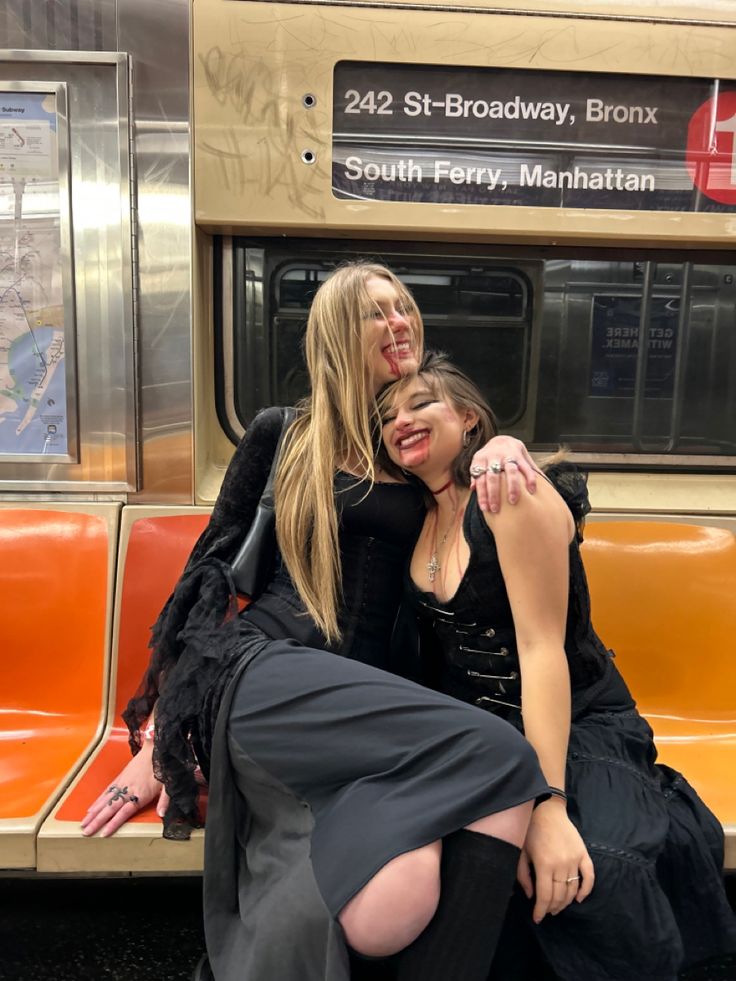 two women sitting on a subway car with their arms around each other's shoulders