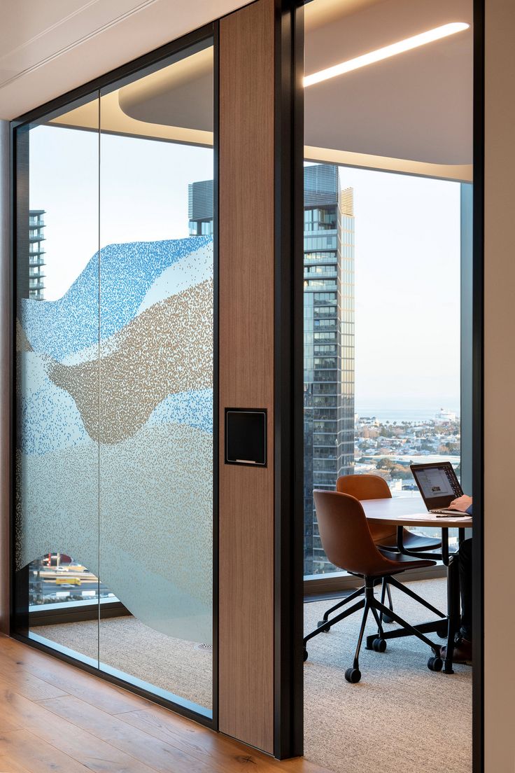 an office with glass walls and desks in front of large windows overlooking the city