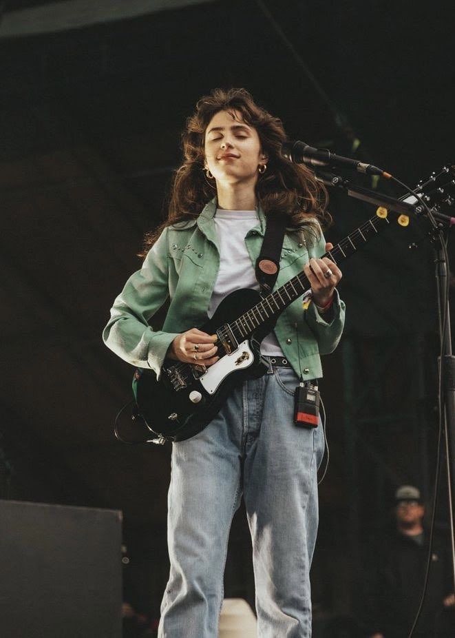 a woman standing in front of a microphone holding a guitar