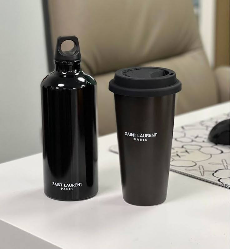 two black coffee cups sitting next to each other on a white counter top in front of a chair