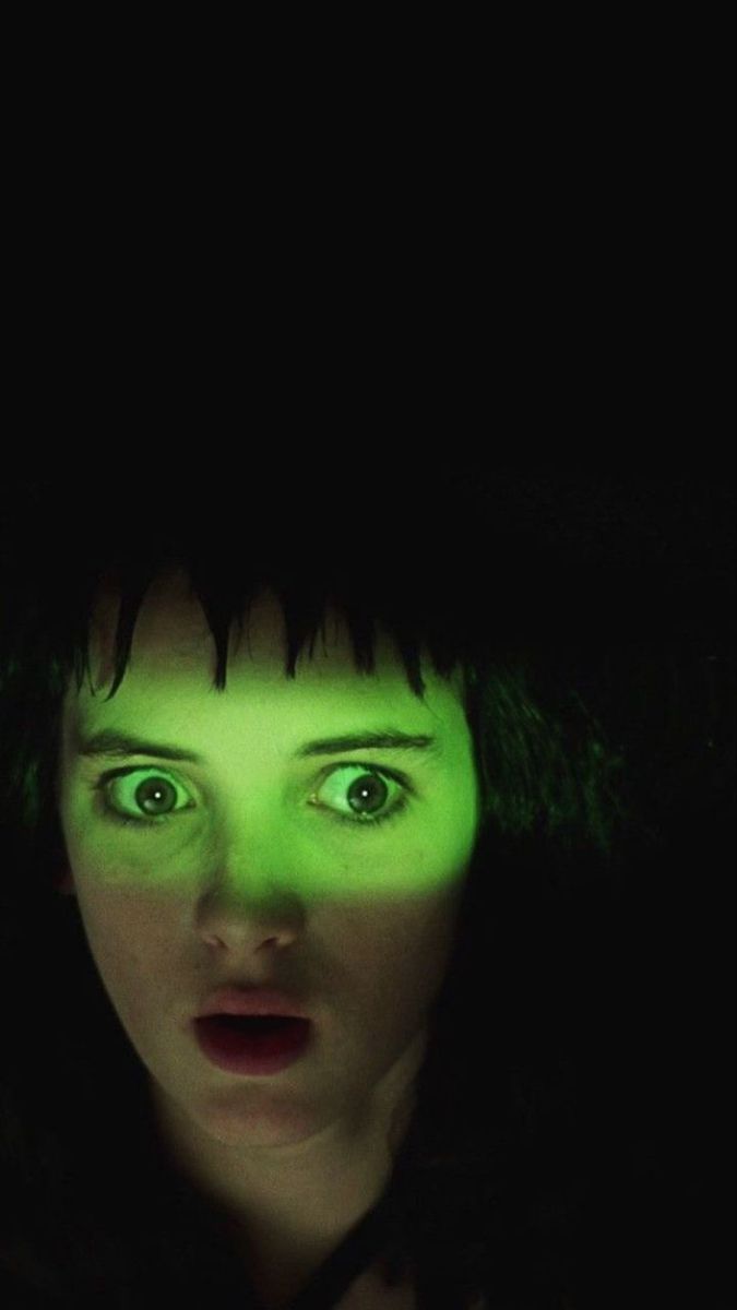 a woman with green eyes and black hair looking at the camera in the dark,