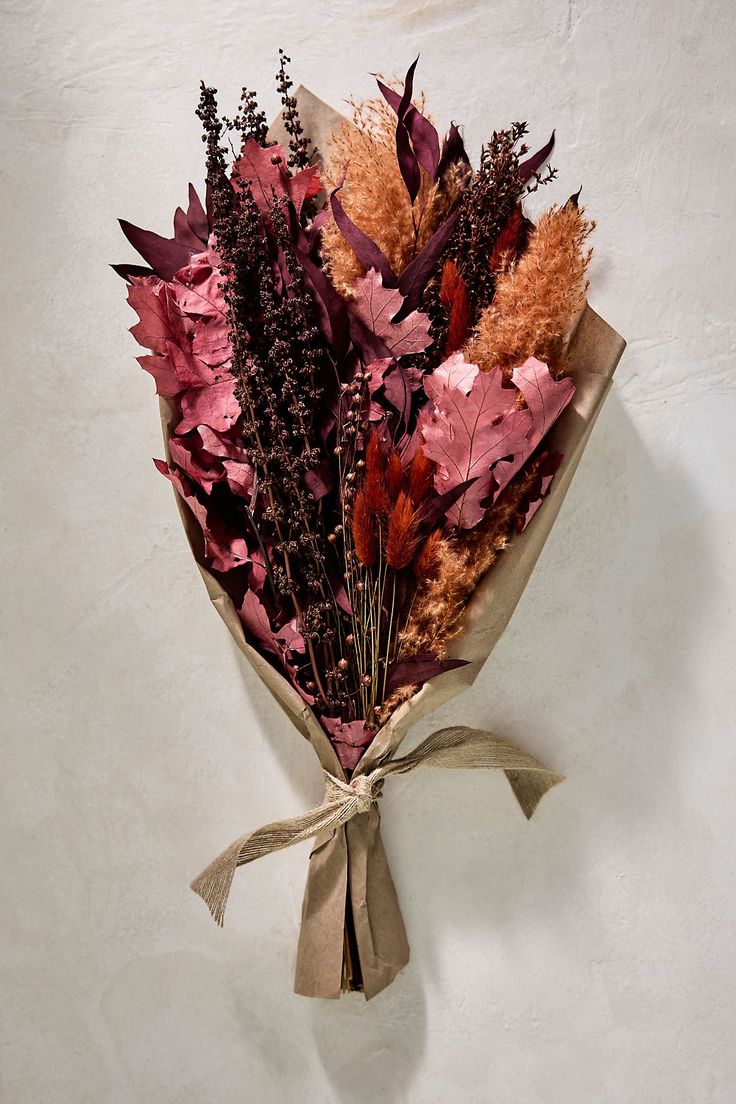 a bouquet of dried flowers wrapped in brown paper on a white surface with a ribbon