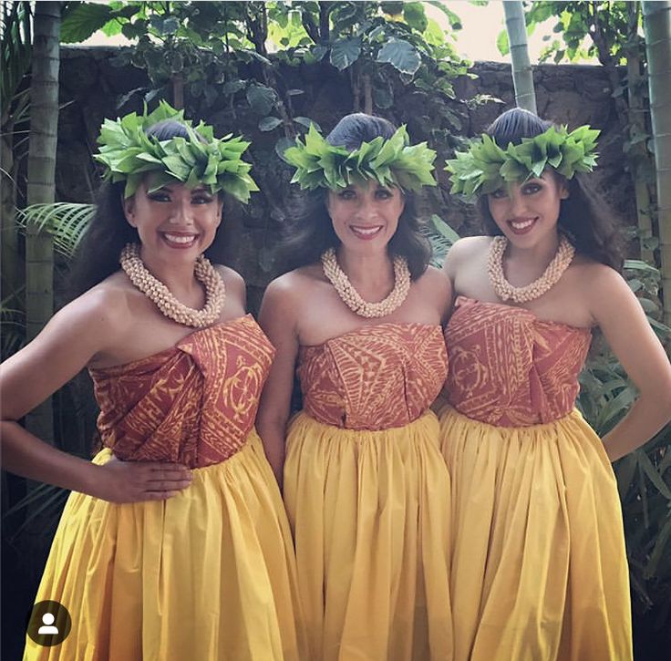 three women in yellow dresses standing next to each other with green plants on their heads