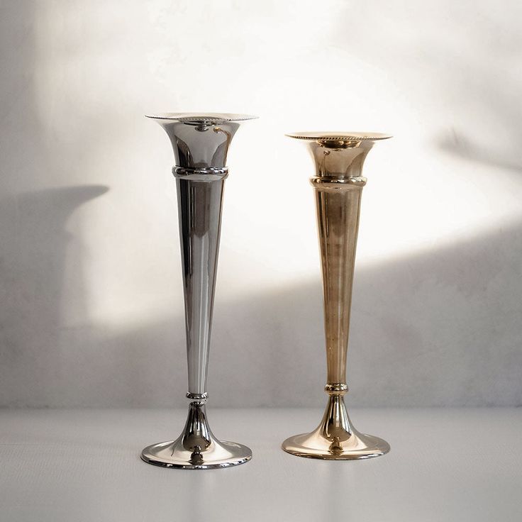 two silver vases sitting side by side on a white counter top, one is gold and the other is silver