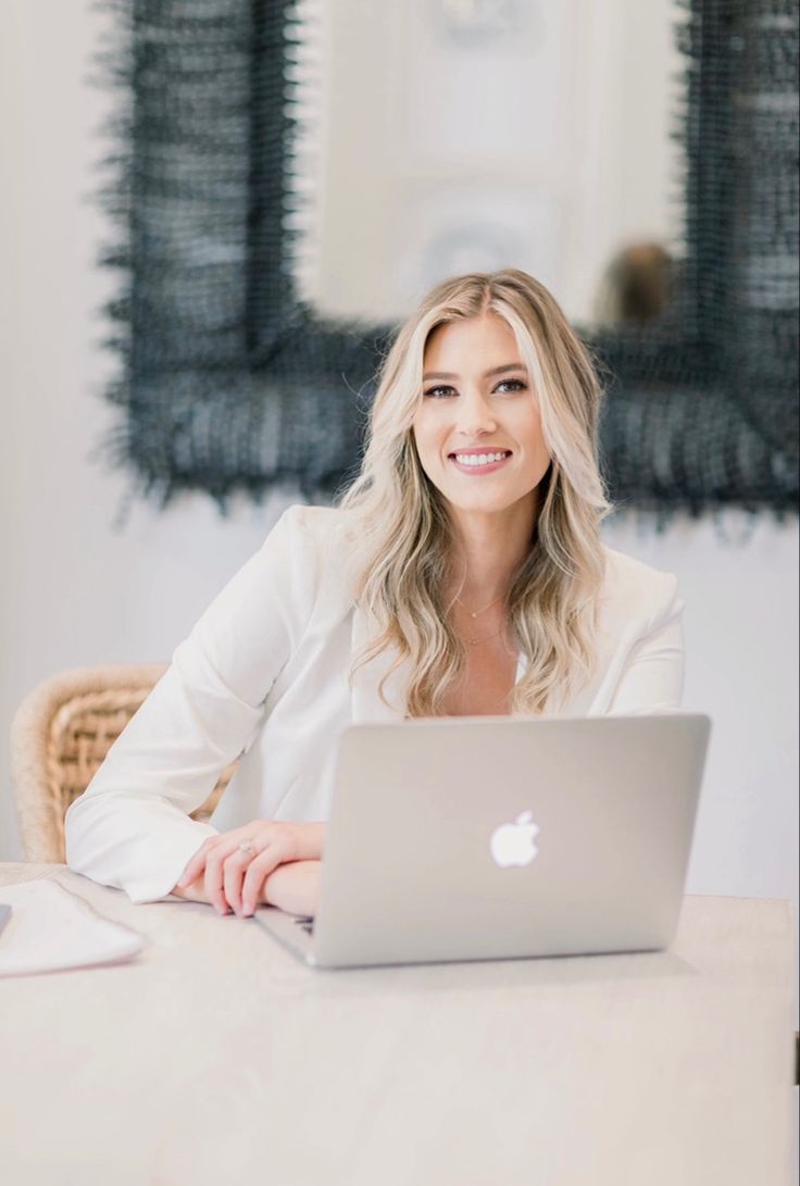 a woman sitting at a table with a laptop in front of her, smiling for the camera