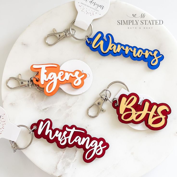 four keychains with different colors and designs on them sitting on a marble surface