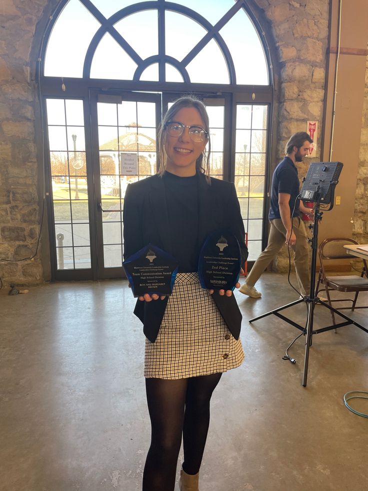 a woman standing in front of a window holding up two award plaques on her hands