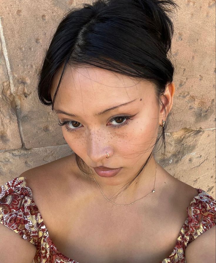 a young woman with freckles on her face looking at the camera while standing in front of a stone wall