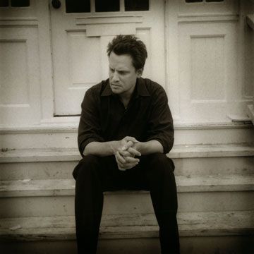 a man sitting on the steps in front of a door with his hands clasped to his knees