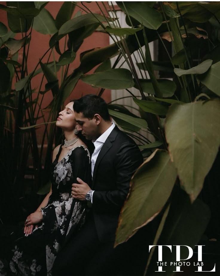 a man and woman standing next to each other in front of plants