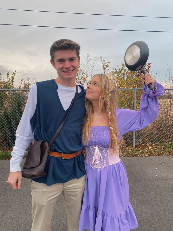 a man standing next to a woman wearing a purple dress and holding a light bulb