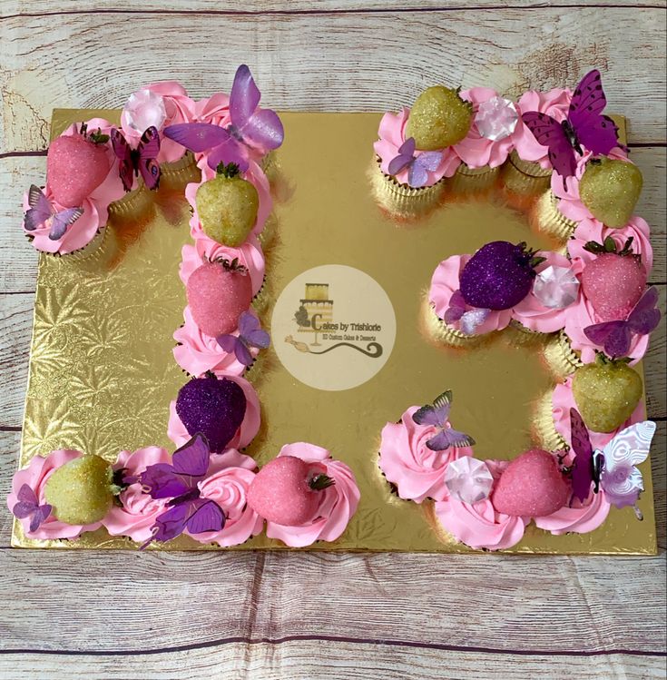 cupcakes decorated with pink frosting and purple flowers on a gold card board