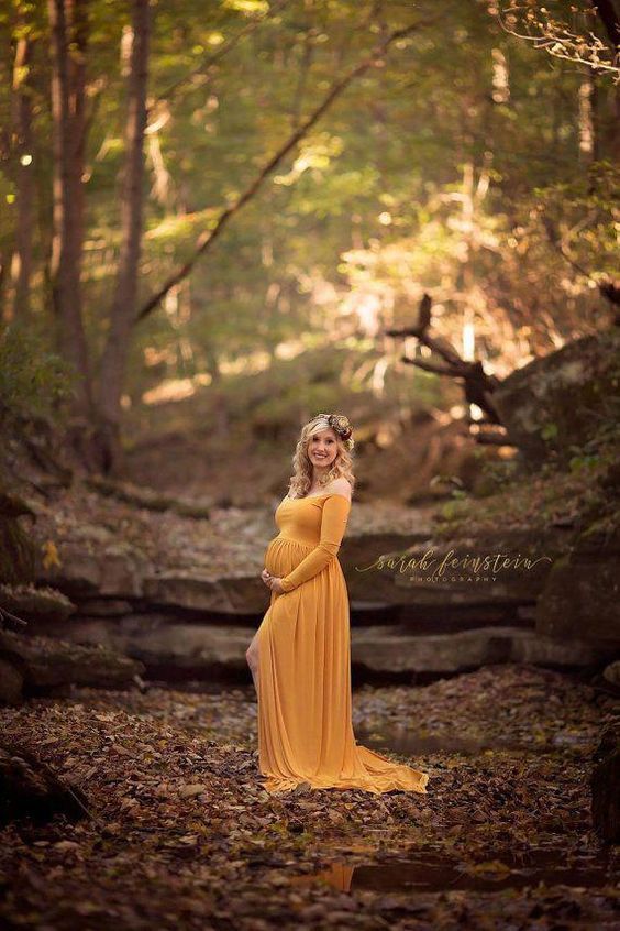 a pregnant woman in a yellow dress standing in the woods with her hands on her hips