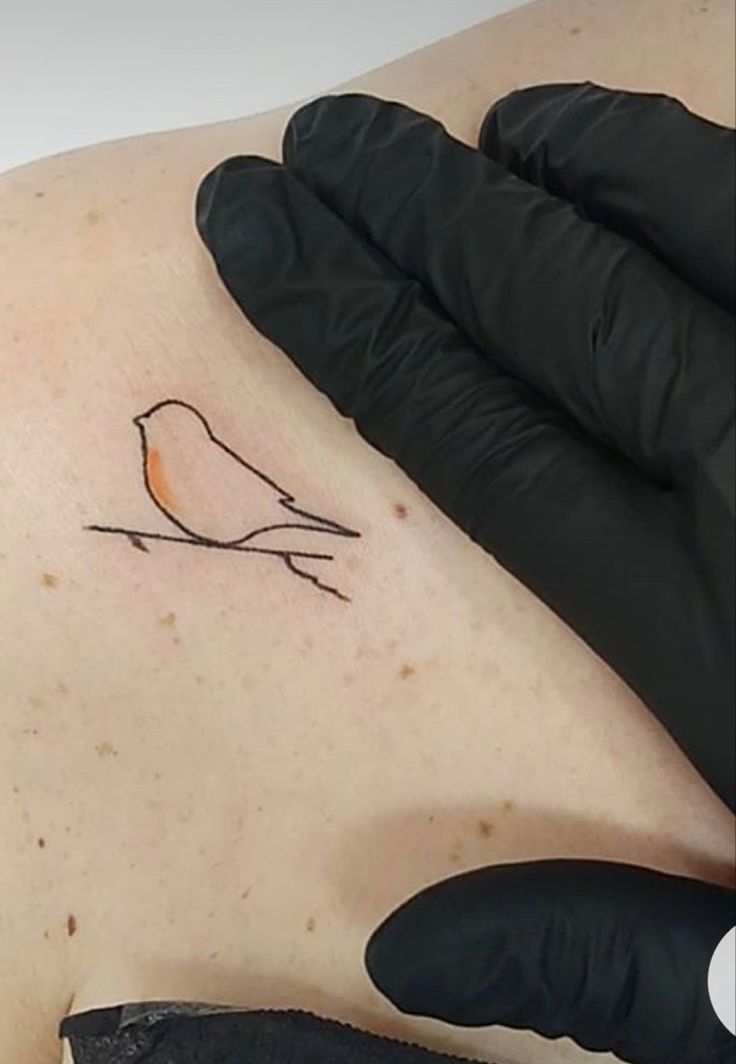 a small bird tattoo on the back of a man's left shoulder and arm