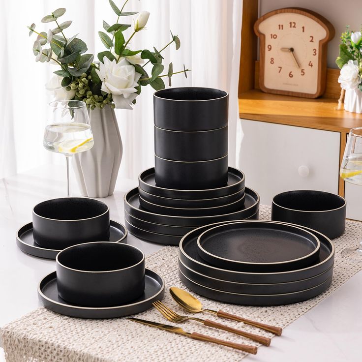 a table topped with black plates and silverware next to a vase filled with flowers