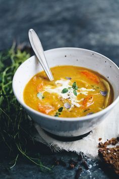 a white bowl filled with soup next to bread and sprig of parsley