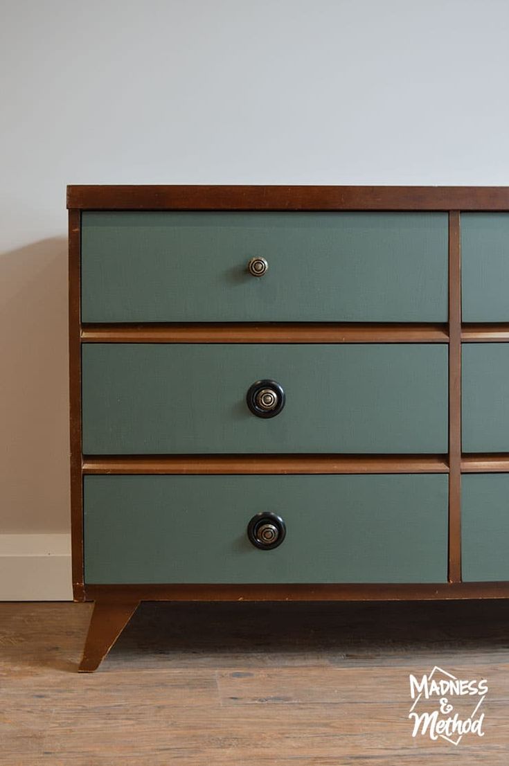 a green dresser with three drawers and two knobs on each drawer, in front of a white wall