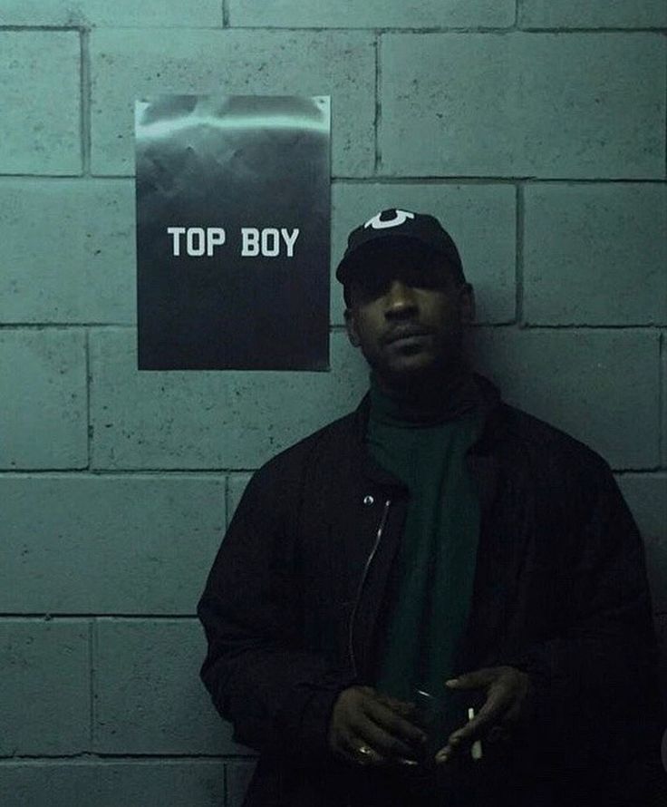 a man standing in front of a wall with a sign on it that says top boy