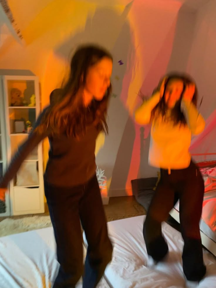 two women dancing on a bed in a room with walls painted pink and yellow,