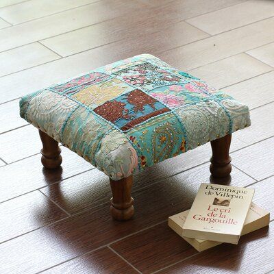 a patchwork foot stool next to a book on the floor