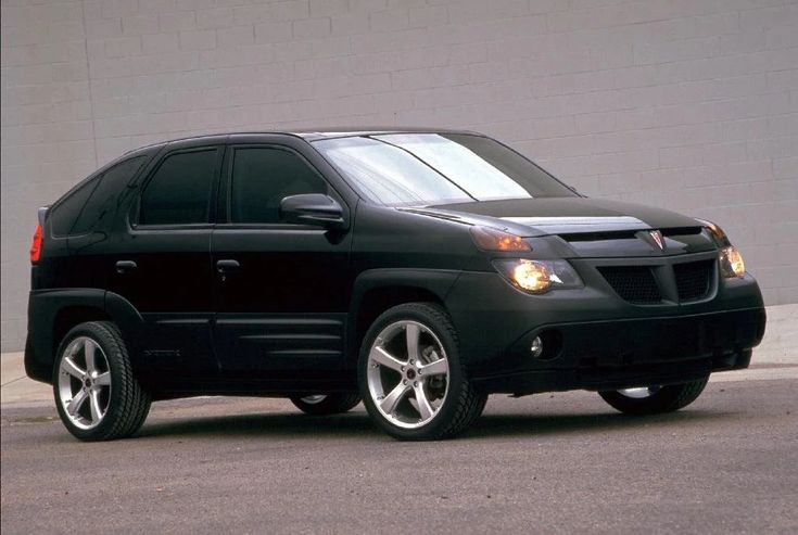 a black suv is parked in front of a gray wall and has white rims