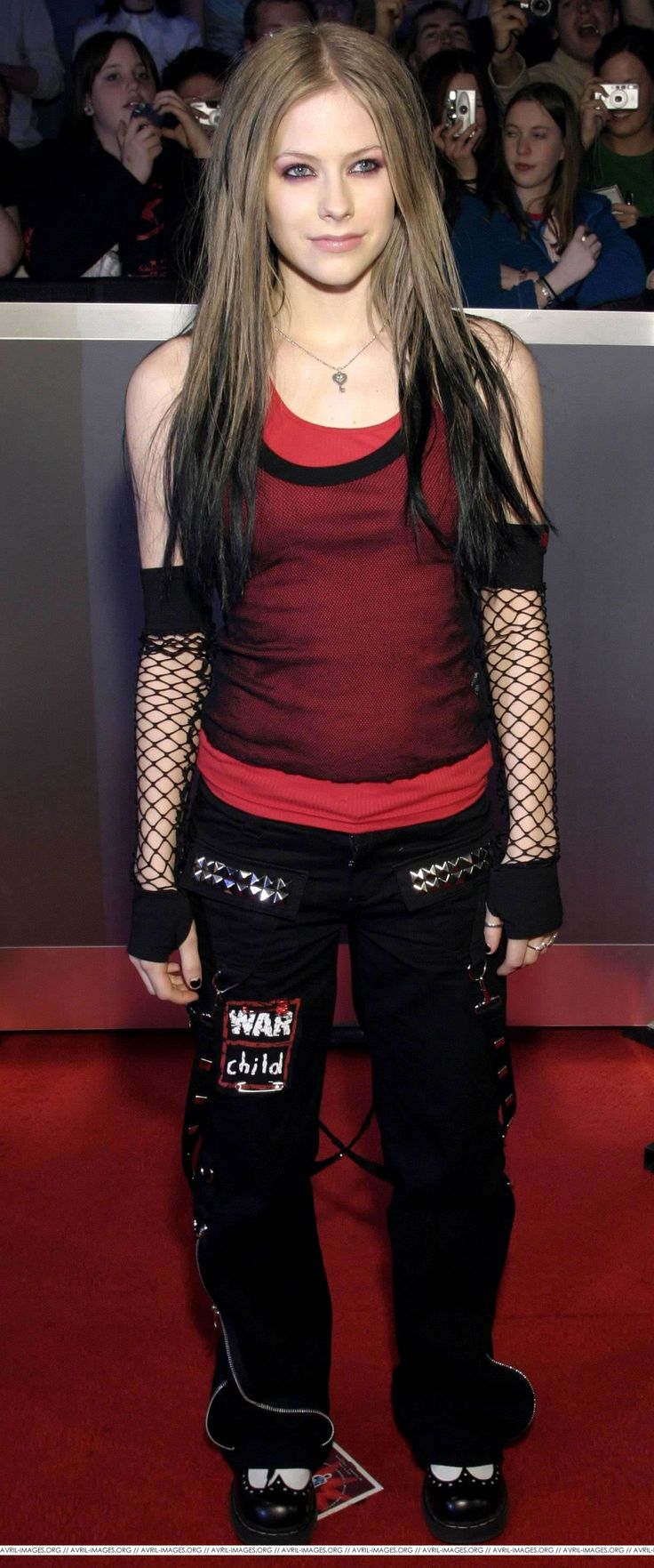 a woman with long hair wearing black pants and red shirt standing in front of a crowd